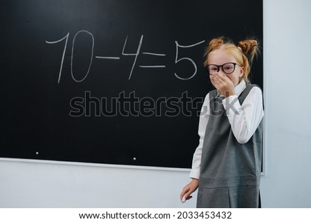 Amused giggling girl solving a basic math equasion on a blackboard in a class. She's made a mistake.