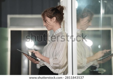 Amusement flickers over her profile while she reads, the luminous sphere and green tinted panes wrapping the elegant evening frame around her figure in a bright modern coworking office.