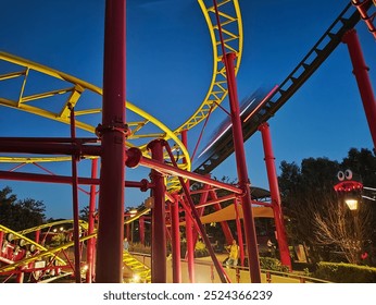 An amusement park roller coaster bathed in night lights, with bright yellow and red tracks. The contrast of neon lights against the deep blue sky highlights the excitement and thrill of the ride - Powered by Shutterstock