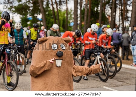 Amusing beaver plush mascot character pointing with finger next to cyclists