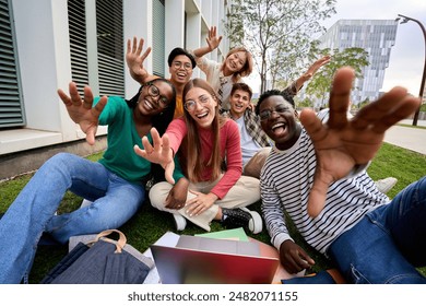 Amusing portrait of group of diverse young friends excited waving at camera with hands sitting on campus grass. Generation z of happy students gathered posing together for photo outside faculty class - Powered by Shutterstock