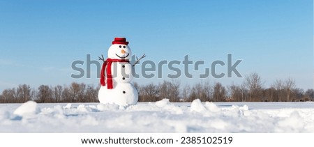 An amusing snowman, adorned with a trendy red hat and red scarf, graces a snow-covered field with a backdrop of brilliant blue skies. Christmas postcard