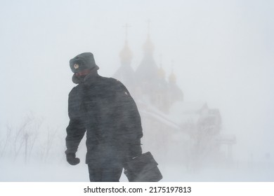 Anadyr, Chukotka, Russia - February 25, 2011. A Russian Policeman Walks Through The City During A Heavy Snowstorm. Windy And Snowy Weather. Snow Storm In The City. In The Distance Is The Cathedral.