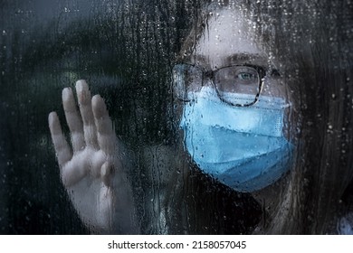 ANAHEIM, UNITED STATES - May 02, 2022: A Girl With A Mask Behind The Window On A Rainy Day As A Concept Of A Pandemic Fatigue