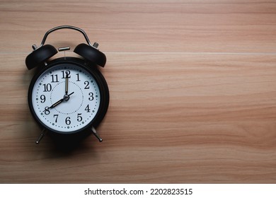 Analog alarm clock is placed on wooden table, Empty space for text.
