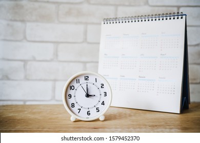 analog clock with blurred calendar  on wooden table