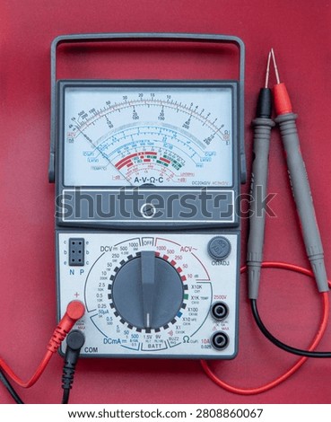 Analog multimeter with test probes isolated on red background 