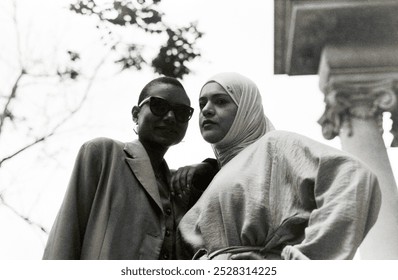 Analog portrait of multicultural couple of female friends posing with confidence. They are multiethnic friends, one is a muslim woman wearing hijab and the other has short hair and sunglasses. - Powered by Shutterstock