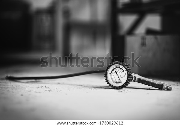 Analog tire\
pressure gauge with a hose lying on the ground of a car repair shop\
- black and white version of\
photo.