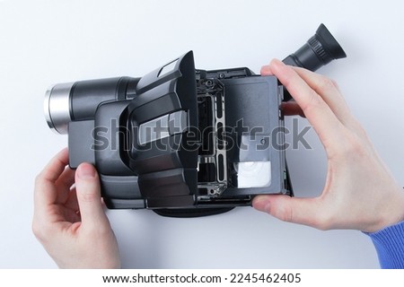 An analog VHS standard video camera and a video cassette in the hands of a caucasian woman. White background. View from above.
