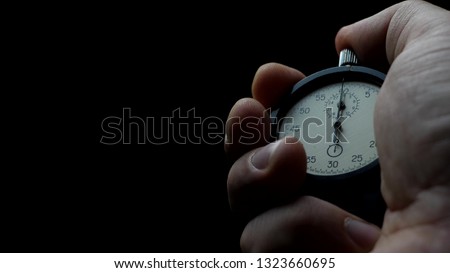 Analogue stopwatch in hand on the black background. Time start with old chronometer. Man presses start button in the sport concept