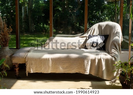 Analytical couch positioned against an open window overlooking a garden, used by psychotherapist treating patient with mental illness. 
