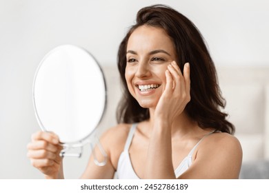 Analytical millennial woman focused on skincare, closely examining her eyes in a bathroom, anti-ageing skin care - Powered by Shutterstock