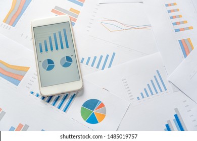 Analytics graph and pie chart on mobile phone and many accounting data on paperwork documents. Modern business workplace or technology concept.