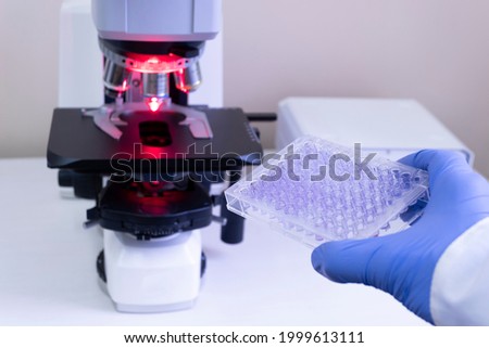 To analyze samples on a large microscope, the doctor holds an immunological tablet in his hand against the background of a microscope.