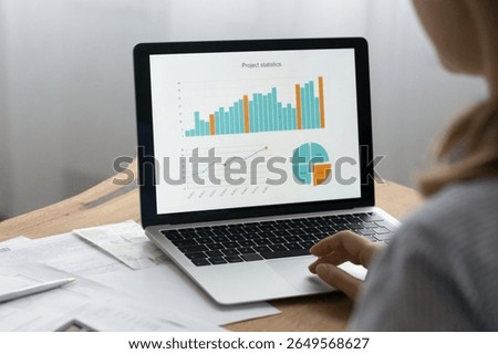 Analyzing data. Close up over shoulder view of young businesswoman preparing financial report managing project statistics counting in laptop business application. Focus on charts graphs on pc screen