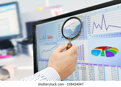 Analyzing Data On Computer Male Hand With Magnifying Glass Over Financial Data And Charts On Computer Screen