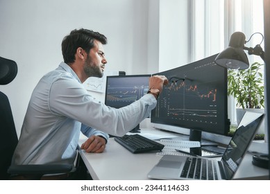 Analyzing data. Thoughtful young trader is pointing at graphs on computer screen while working in his modern office.