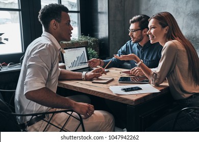 Analyzing Fresh Data. Group Of Young Confident Business People Discussing New Project And Smiling While Spending Time In The Office