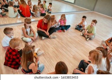 Analyzing Mistakes. A Group Of Little Dancers Sitting On The Floor Gathered Around Their Female Dance Teacher And Listening Her Carefully. Dance School. Relationship Between Teacher And Kids