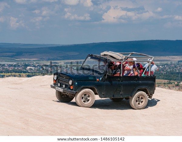 Anapa, Russia - August 7, 2019 - SUV cabriolet with\
happy happy passengers standing on a rock near the clear blue sky\
of the black sea