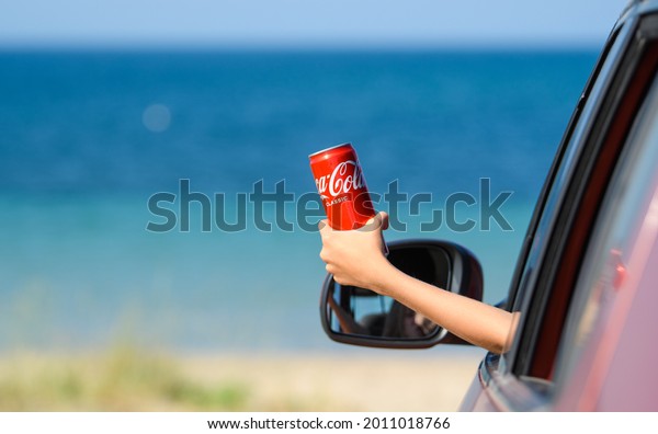 Anapa, Russia - July\
2021: A girl in a car on the seashore holds a can of delicious\
Coca-Cola in her hand.