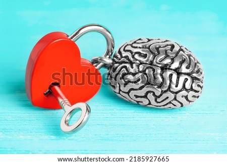 Anatomical copy of a human brain attached to a red heart-shaped padlock with a key isolated on blue wooden background. Brain affections control concept.