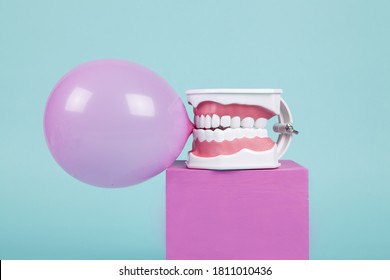 An Anatomical Plastic Tooth Model To Learn How To Brush Teeth Holding A Chewing Gum Ball On Coloured Cubes. Offbeat Humor And Pop Atmosphere. Minimal Color Still Life Photography 