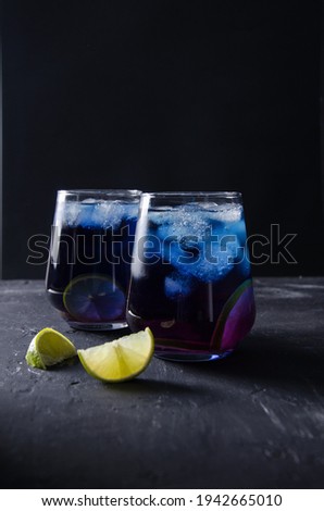 Anchan, butterfly cold drink. Cold blue tea with pieces of ice and lime in a transparent glass on a black background in a dark key, the concept of a cool drink, vertical background, selective focus