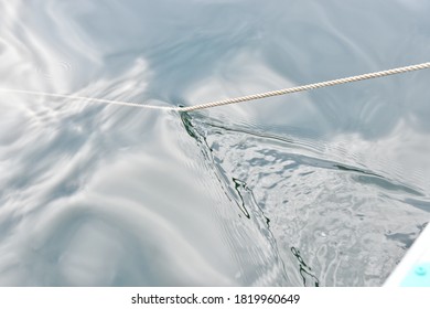 An Anchor Rope Cuts Through Calm Surface Water Creating A Contrasting Wake Of Turbulence. Copy Space.