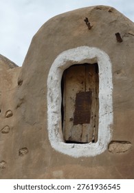 An ancient adobe structure features a rough-hewn wooden door set within a white-washed, irregular opening, hinting at a rich history and unique architecture