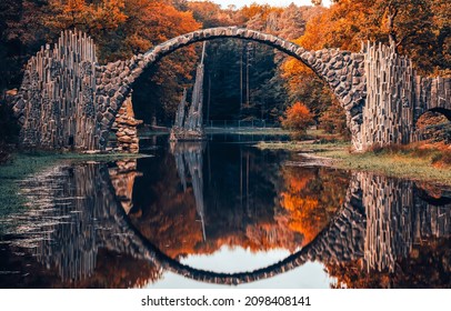 Ancient arched bridge over the river in the autumn forest. Arched bridge reflected in water. Bridge reflection in water. Autumn forest river bridge