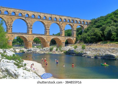 Ancient Arches Of Pont Du Gard And People Swimming On The River Near Nimes, France