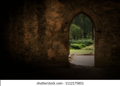 Ancient Archway Frames Summer Garden Beyond.  Thought Provoking Image With High Contract Is Colours.