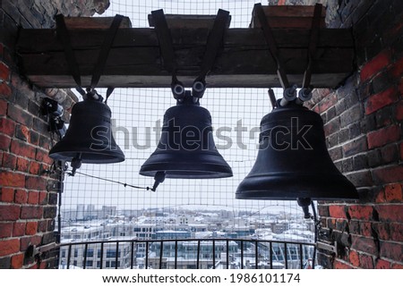 Ancient bells in an old Russian bell tower. Snow-covered modern houses in the distance somewhere below. Shot at Epiphany Cathedral, Kazan, Russia