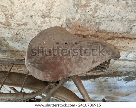 Ancient bicycle saddles were made of hard leather, looked dirty and had rusty iron springs. leaning against an old wall
