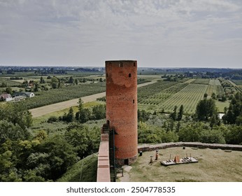 Ancient brick tower stands tall amidst lush green fields and trees, under a clear blue sky. The serene landscape evokes a sense of history and tranquility, perfect for rural and historical themes. - Powered by Shutterstock