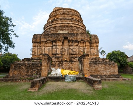 Ancient Buddhist stupa at Ayutthaya Historical Park, Thailand, with cloth-covered Buddha statues at its base amidst ruins.