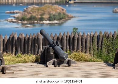 ancient cast-iron cannon on a wooden gun carriage in an open-air museum. In the background a wooden palisade and the surface of a wide river