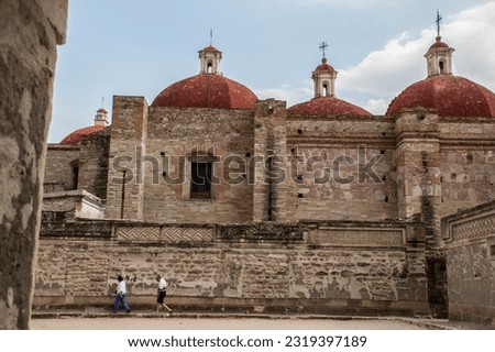 Ancient catholic church with stone walls and domes and two people walking in front of it. San Pablo church in the Magical Town of Mitla, Oaxaca, Mexico. 