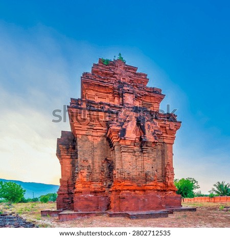 Ancient Cham tower in Ninh Thuan, Vietnam, standing against a dramatic sunset sky with surrounding mountains. A remarkable historical and cultural landmark showcasing the architectural heritage of the Cham civilization in Southeast Asia.