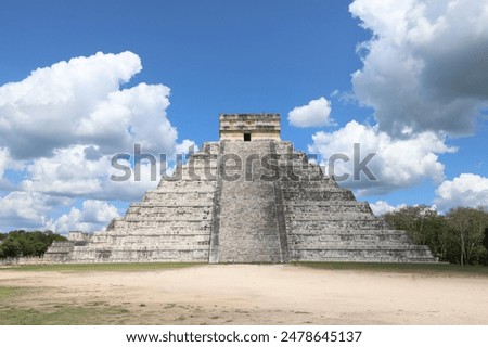 An Ancient Chichen Itza Pyramid located in Yucatan Mexico. Front view of pyramid without people surrounded by fluffy white clouds and blue sky.
