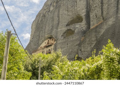 Ancient cliffside monastery peeking through lush greenery, etched into the rock face in Meteora, Greece - Powered by Shutterstock
