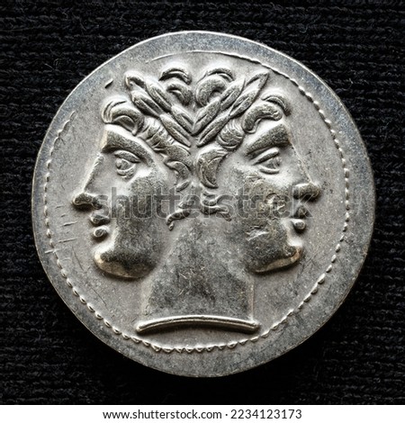 Ancient coin showing two-headed Roman god Janus, 225-214 BC. Old money, silver didrachm isolated on dark background, macro top view. Concept of Rome, vintage coin texture, face, artifact and history.