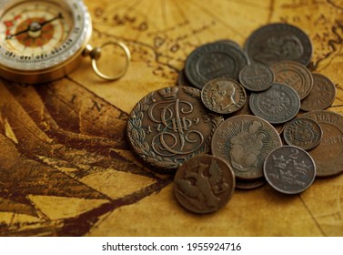 Ancient Coins With A Compass. Metal Money Of Russia And European Countries Against The Background Of An Old World Map.