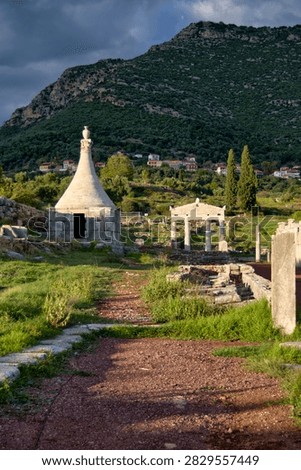 Ancient conical stone funerary monument and Doric gate at an archaeological site in Greece.