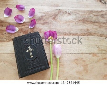 An ancient Danish hymnbook (Psalmer) with prayers and verses. Laying on a wooden table with pink and purple tulips and tulip petals. Communion, church, hope concept - space for text