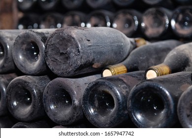 Ancient dark dusty wine bottles aging in underground cellar in rows. Concept winery vault with rare wines, exclusive collection. Stacks of wine bottles resting, laying flat in racks in old cave