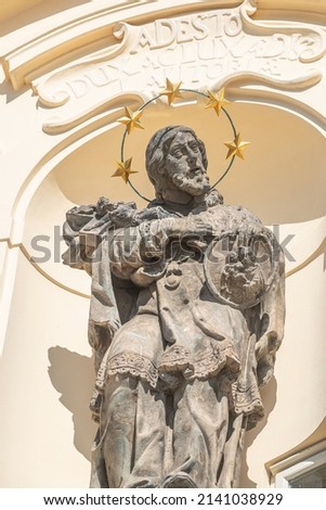 Ancient decorative top facade statue of priest, bishop with nimbus and holding a cross with crucified Christ at small church near Charles Bridge in Prague, Czech Republic, details, closeup