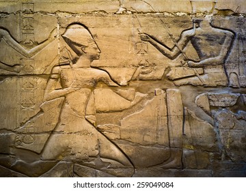 Ancient Egypt Carving Images With Pharaoh And Gods In Karnak Temple. Mythological Story On The Wall - Amun-Ra And Ramses II Kneeling. Travel In Luxor On Famous Architecture Monument.